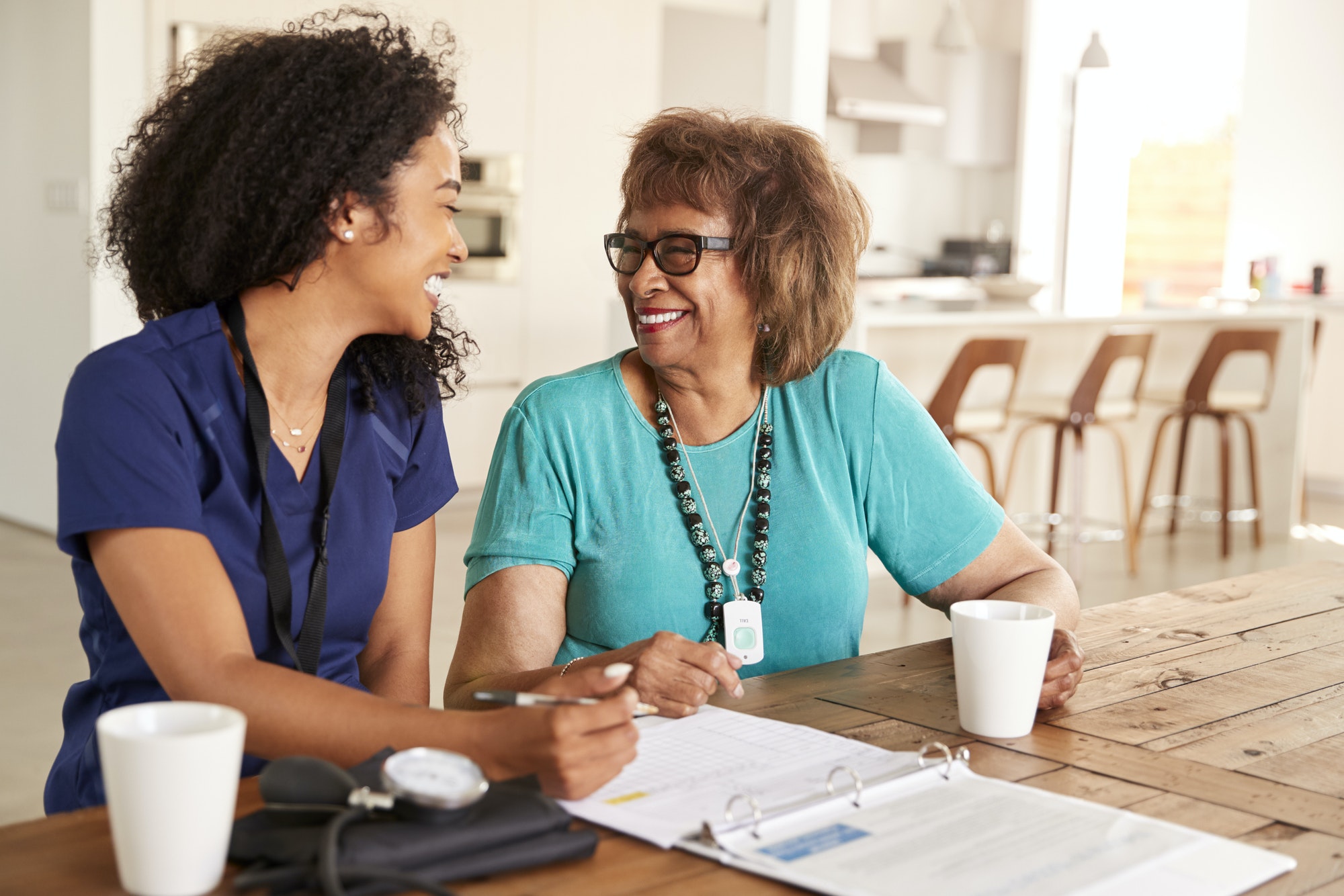 Female healthcare worker sitting at table smiling with a senior woman during a home health visit